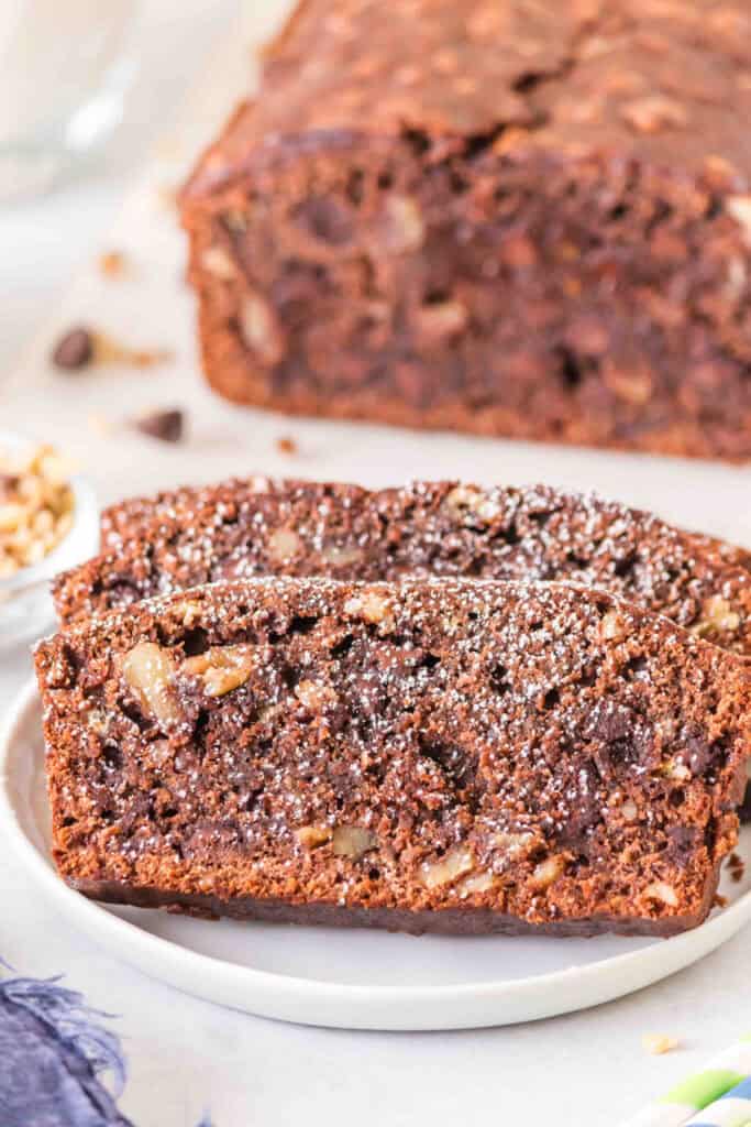Close up of sliced brownie banana bread dusted with powdered sugar on a white plate with a loaf in the background.