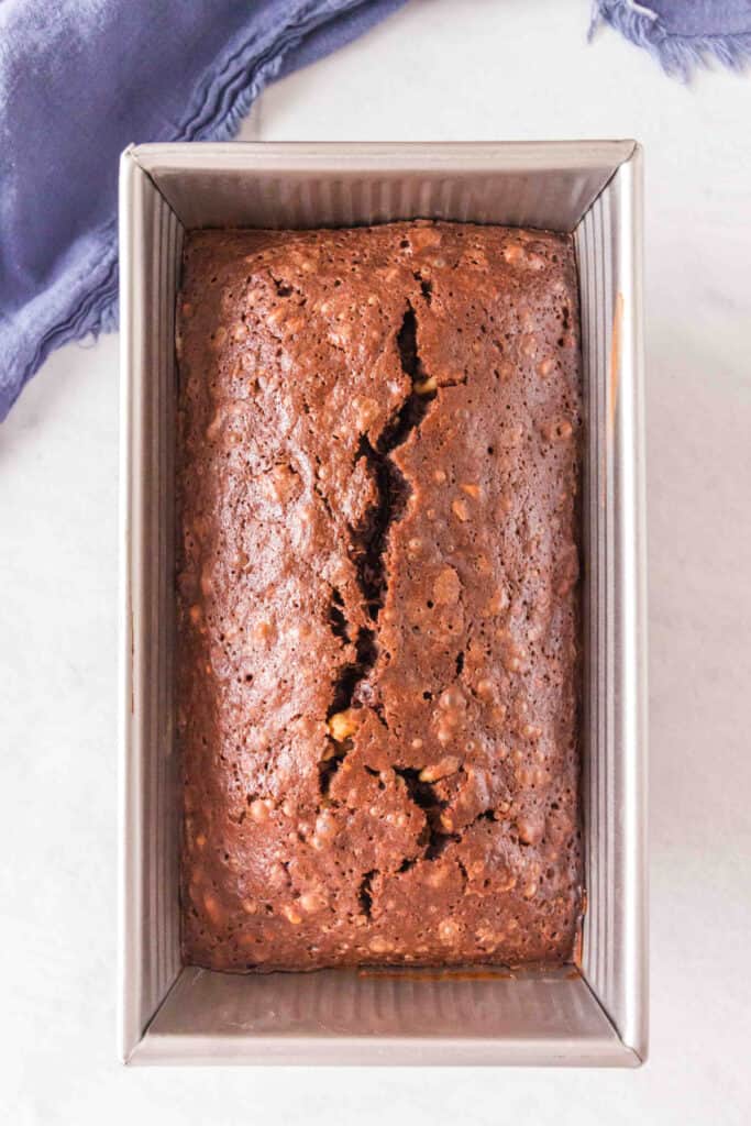 Baked brownie banana bread loaf in a metal loaf pan with a crack down the center.