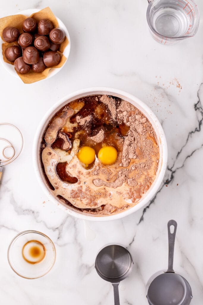 Overhead view of a bowl containing chocolate cake batter ingredients including eggs, milk, oil, vanilla, and cocoa mixture before stirring