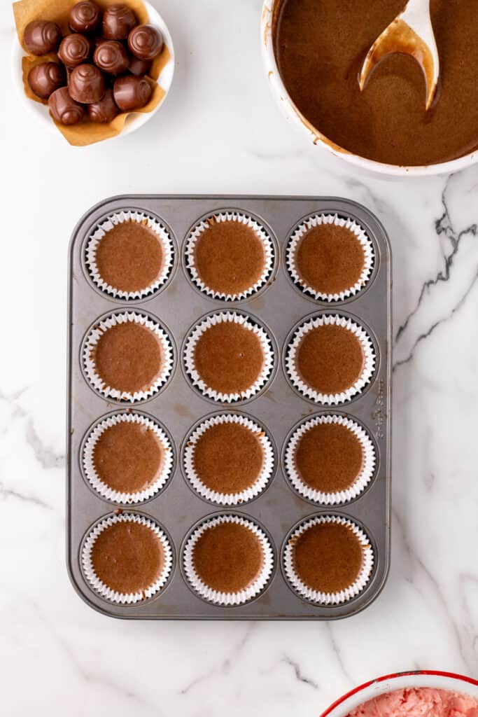 Overhead view of chocolate cake batter poured into lined cupcake wells in a metal muffin pan