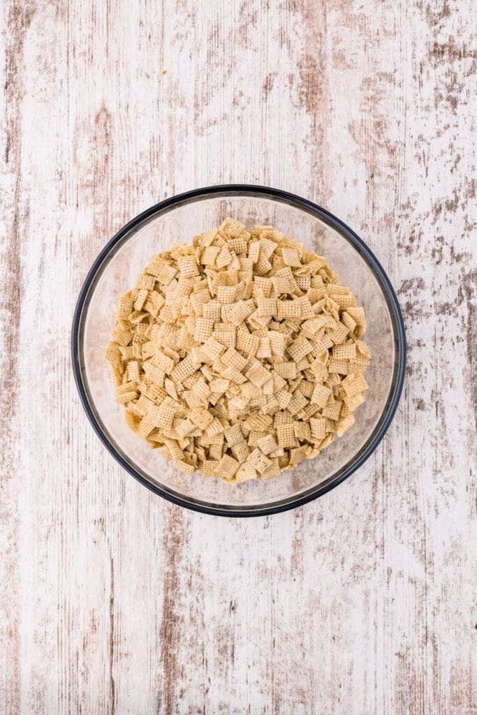 Overhead view of Rice Chex cereal in a clear glass mixing bowl on a white wood surface.