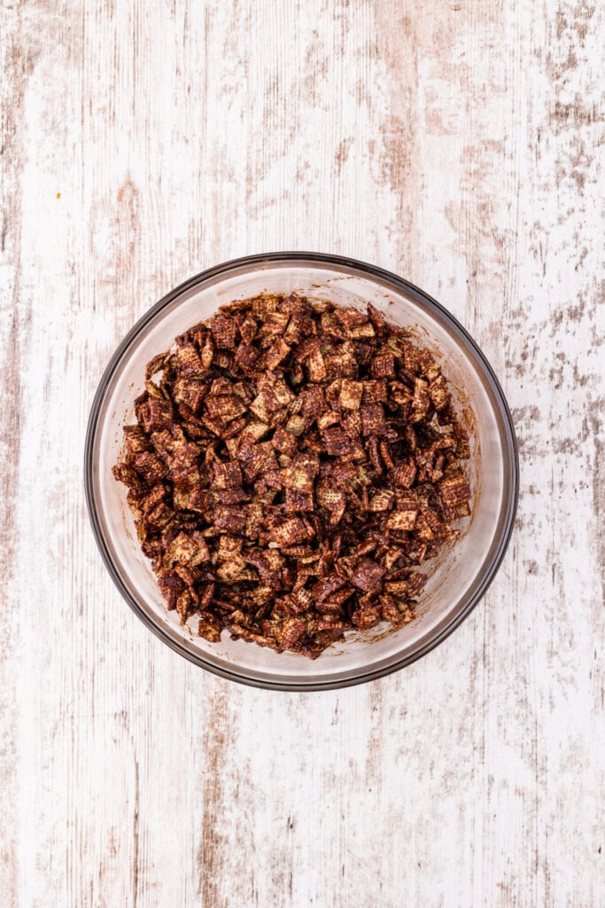 Rice Chex cereal coated in melted chocolate inside a clear glass bowl viewed from above.