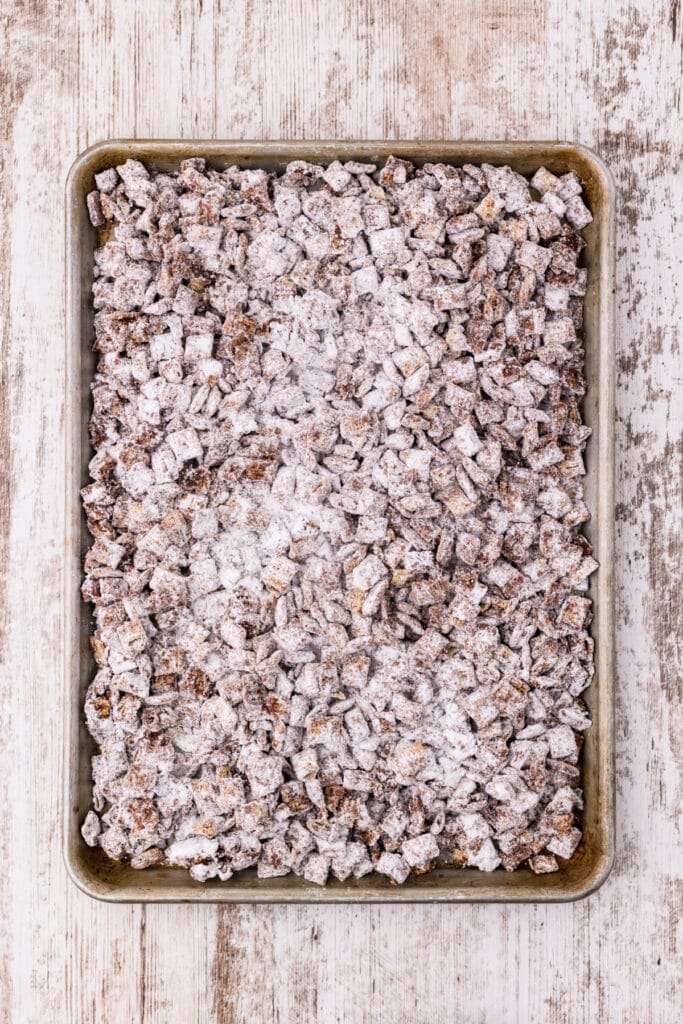 Powdered sugar coated Chex cereal spread evenly in a metal rimmed baking sheet viewed from above.