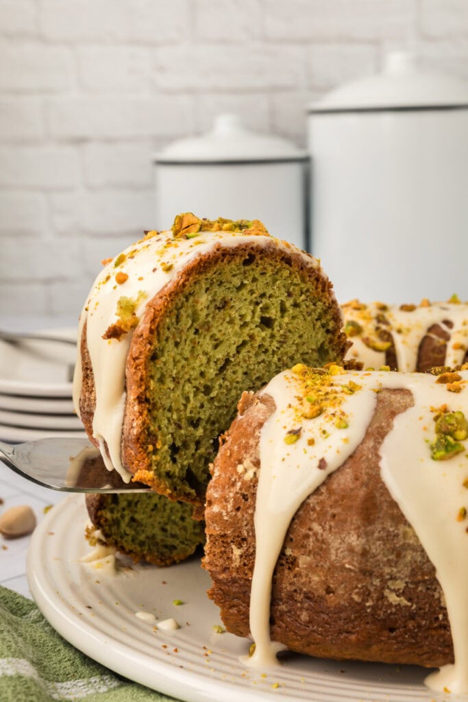 sliced pistachio bundt cake with glaze and chopped pistachios being lefted from cake