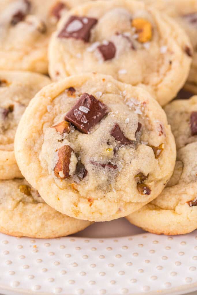 Close up of a pistachio chocolate chunk cookie showing large chocolate pieces and chopped pistachios with coarse salt on top.