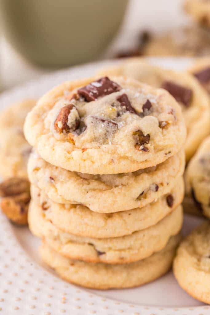 Tall stack of pistachio chocolate chunk cookies on a plate with coarse salt sprinkled on top.