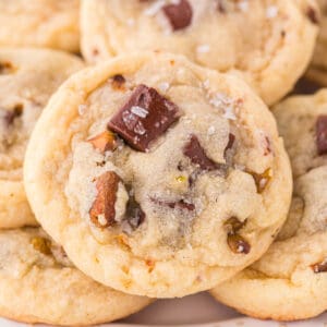 Close up square image of a pistachio chocolate chunk cookie showing chocolate pieces, chopped pistachios, and flaky salt on top.