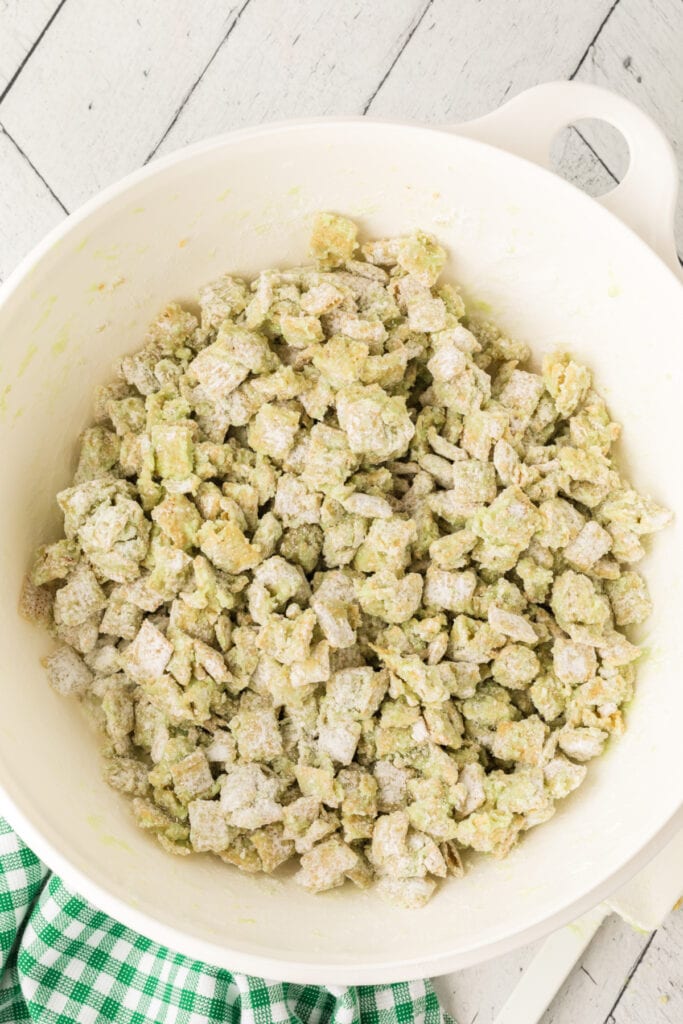 Pistachio muddy buddies fully coated in powdered sugar inside large white mixing bowl