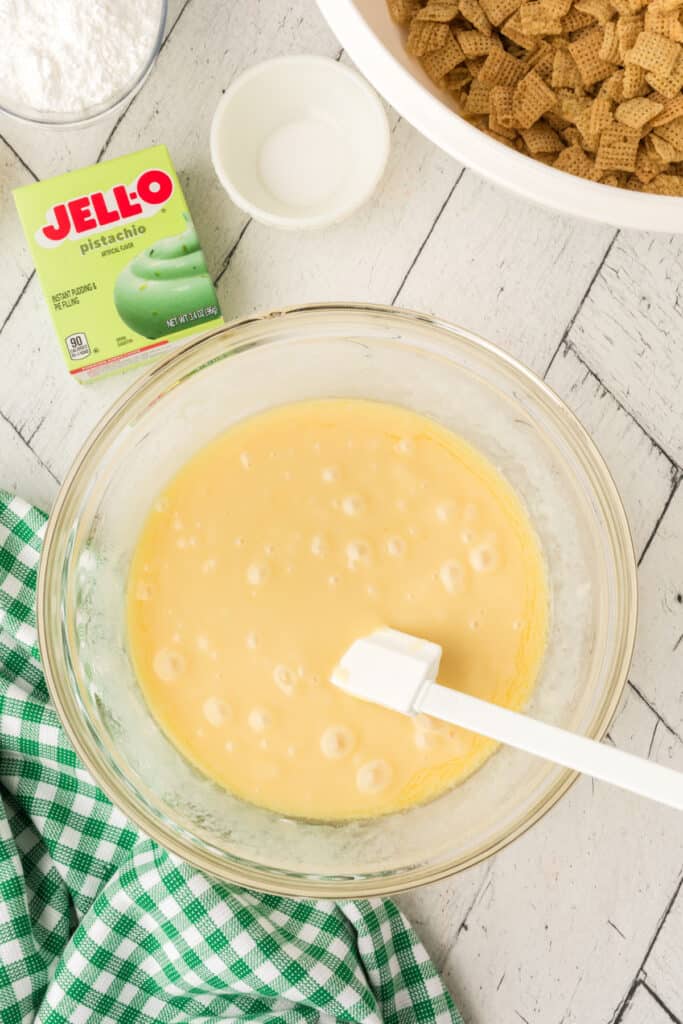 Glass bowl with melted butter and sweetened condensed milk mixture stirred smooth with white spatula