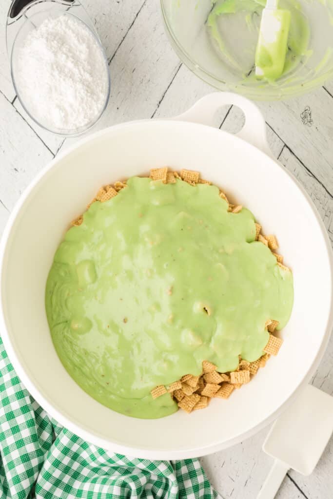 Green pistachio mixture poured over Rice Chex cereal in large white mixing bowl