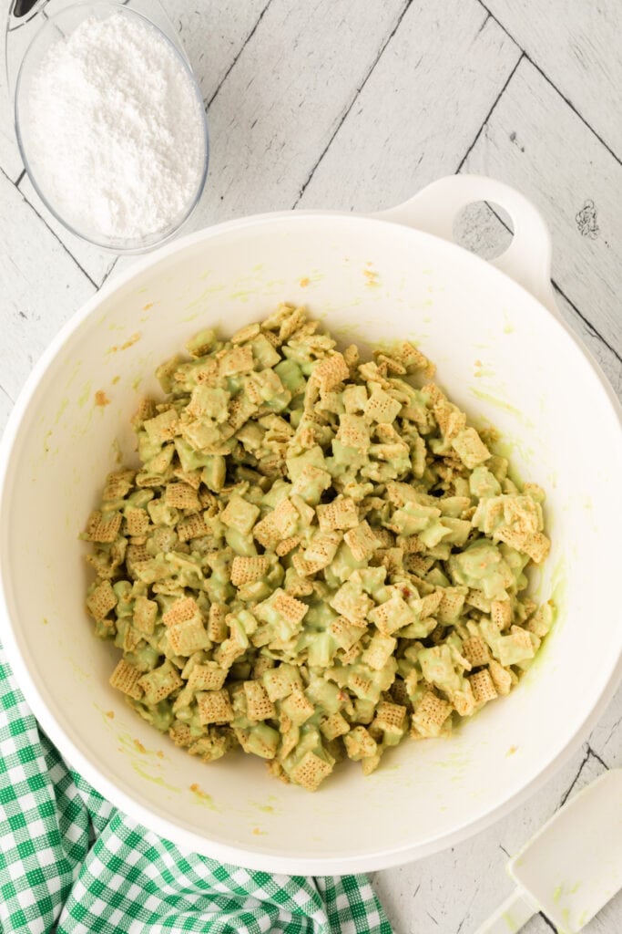 Rice Chex cereal coated in green pistachio mixture inside white mixing bowl