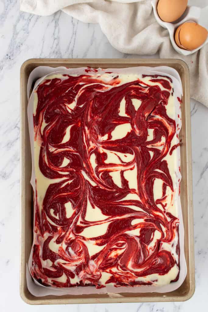 Red velvet and cream cheese layers swirled together in a parchment lined 9x13-inch baking pan before baking