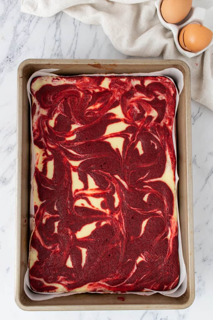 Baked red velvet cheesecake brownies with marbled top in a parchment lined 9x13-inch baking pan