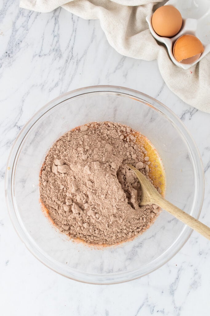 Red velvet cake mix added to melted butter mixture in a glass bowl with a wooden spoon
