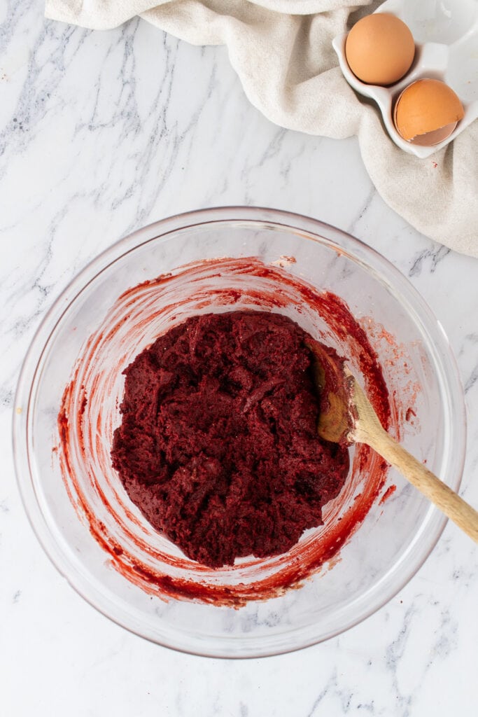 Thick red velvet brownie batter in a glass bowl with a wooden spoon