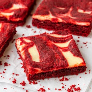 Single square of red velvet cheesecake brownie with cream cheese swirl on parchment paper with crumbs around it