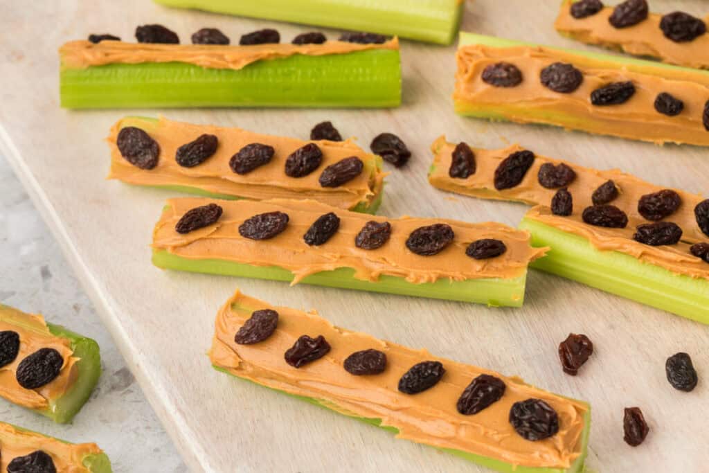 close view of celery sticks with peanut butter and raisins on a wooden board