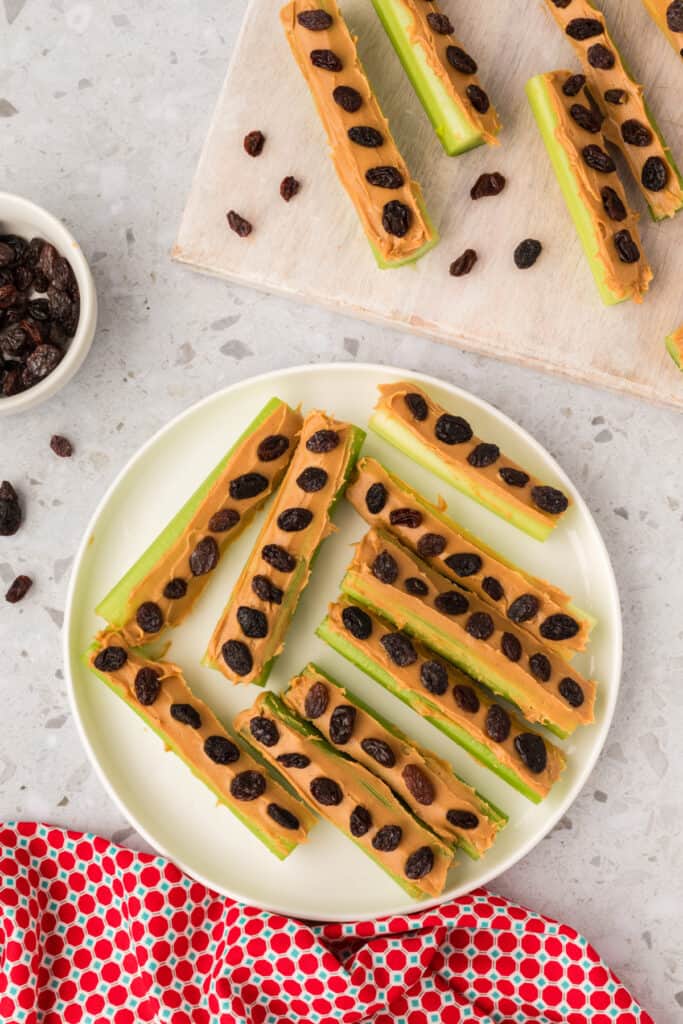 celery sticks topped with peanut butter and raisins arranged on a plate and cutting board