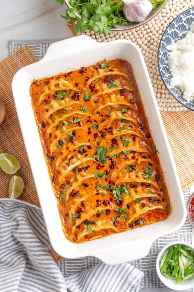 baked dumplings in coconut curry sauce in a white baking dish topped with cilantro and chili crunch
