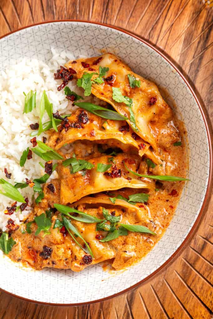 close-up of baked curry dumplings in coconut curry sauce with rice, green onions, cilantro, and chili crunch