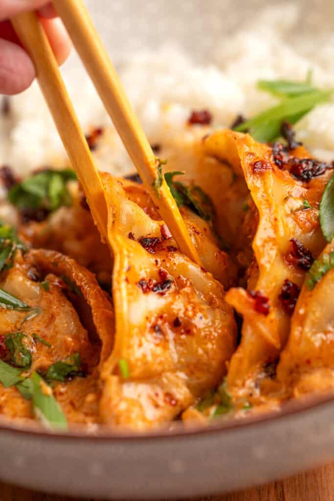 chopsticks lifting a dumpling coated in coconut curry sauce with green onions and chili crunch