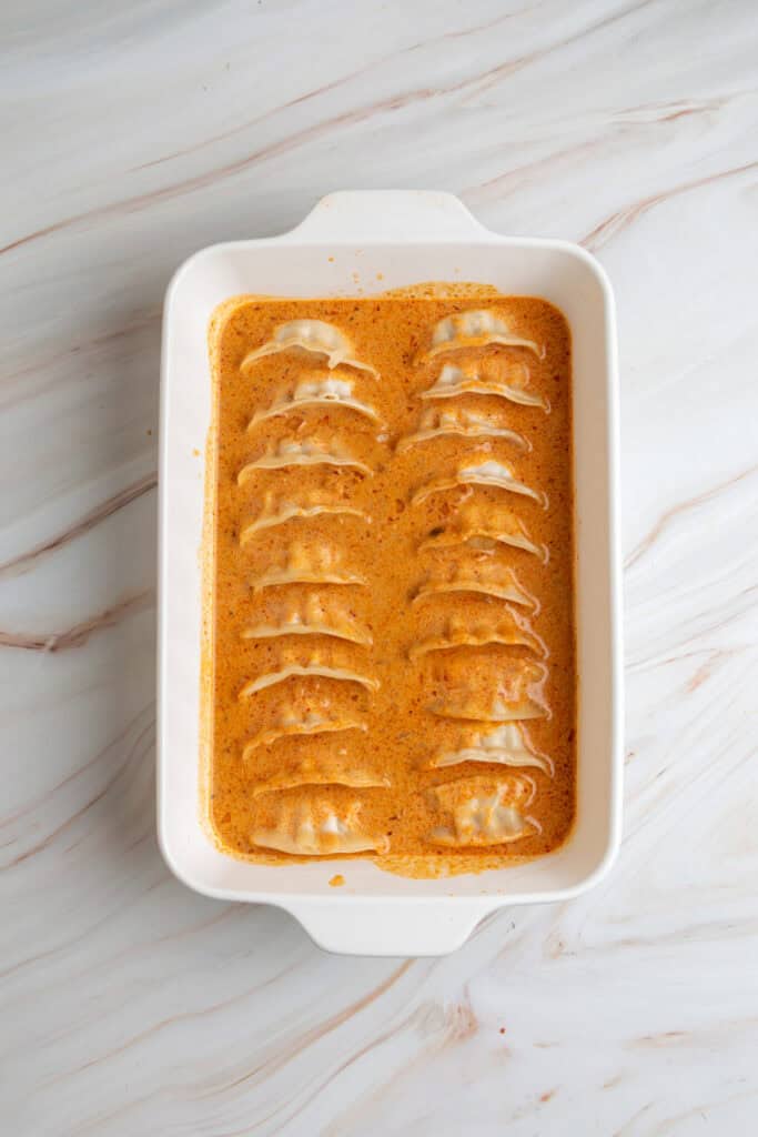 frozen dumplings arranged in a white baking dish covered with orange coconut curry sauce