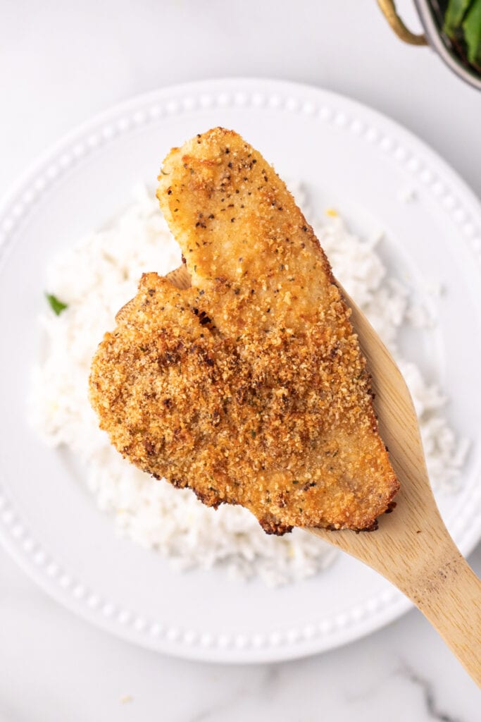 cooked breaded flounder fillet on a wooden spatula over a plate of white rice
