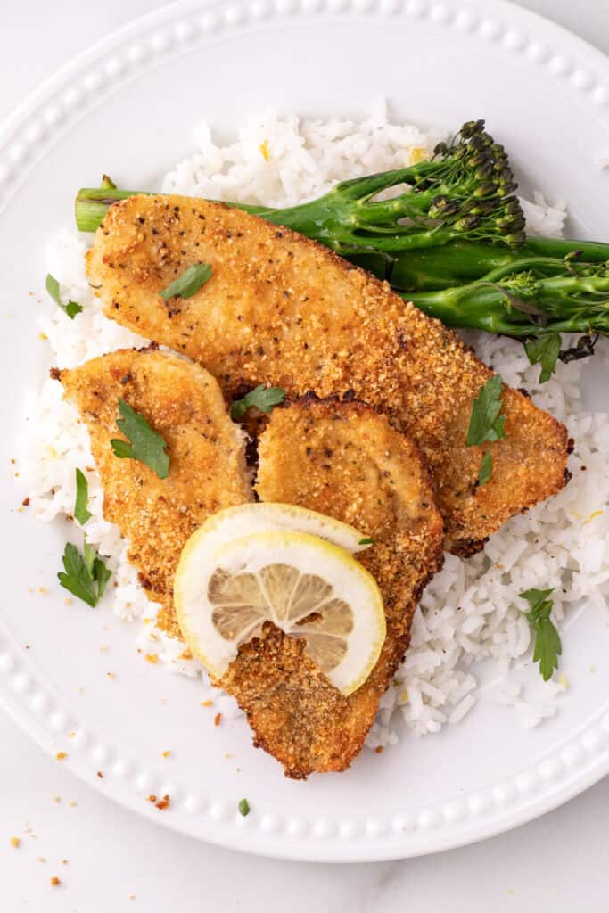 baked garlic parmesan flounder served on white rice with broccolini and a lemon slice