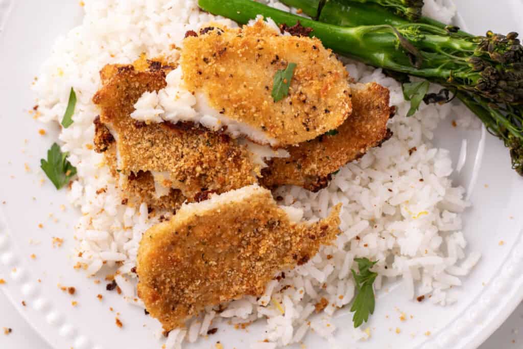 close up of baked garlic parmesan flounder cut open on white rice with broccolini