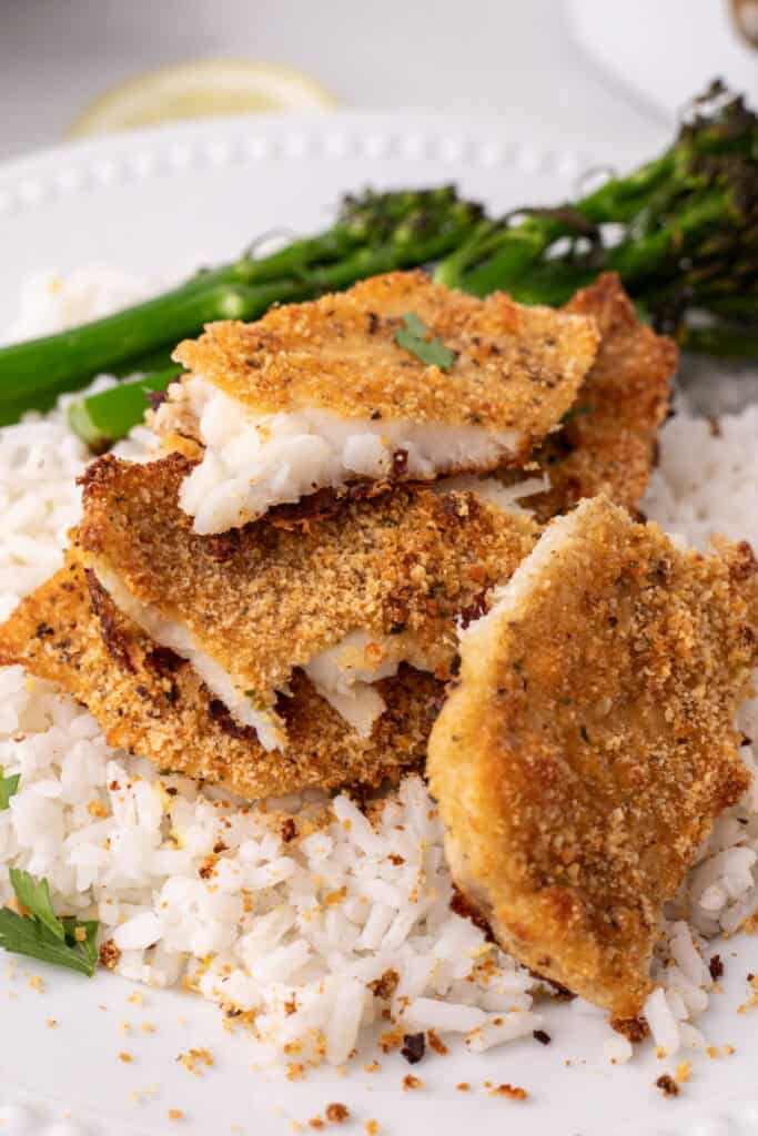 close up of crispy baked garlic parmesan flounder pieces on white rice with crumbs visible