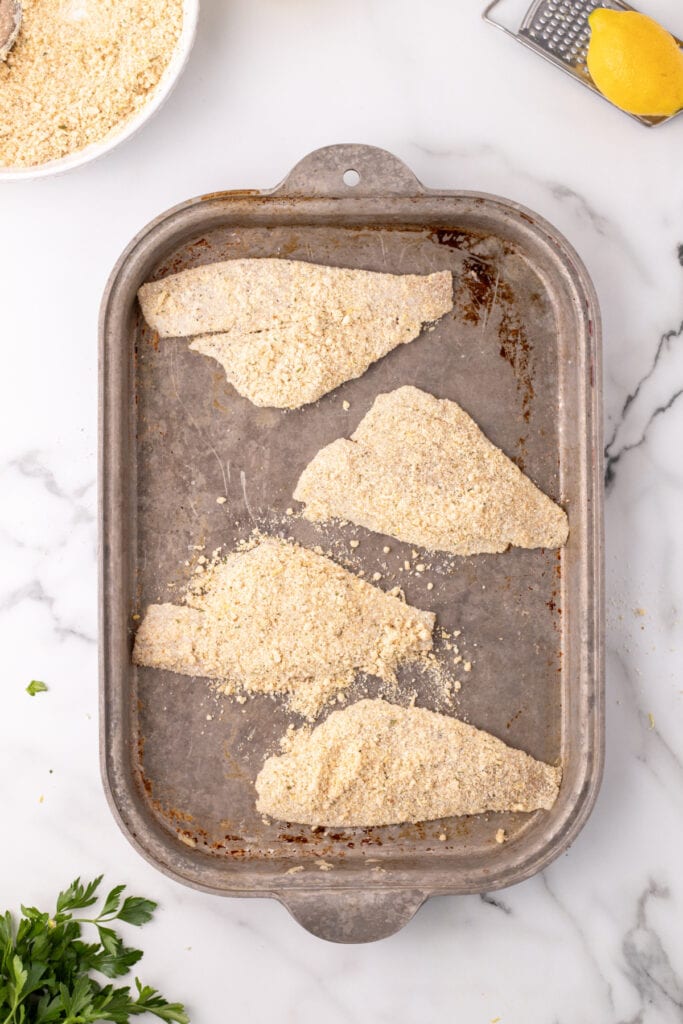 breaded flounder fillets on a baking sheet before baking