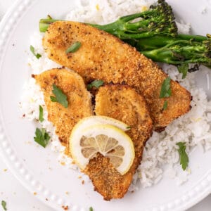 baked garlic parmesan flounder served on white rice with broccolini and a lemon slice on a white plate
