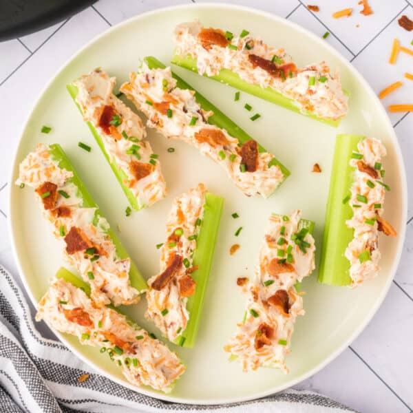 overhead view of cheddar bacon celery sticks on a plate topped with bacon pieces and chopped chives