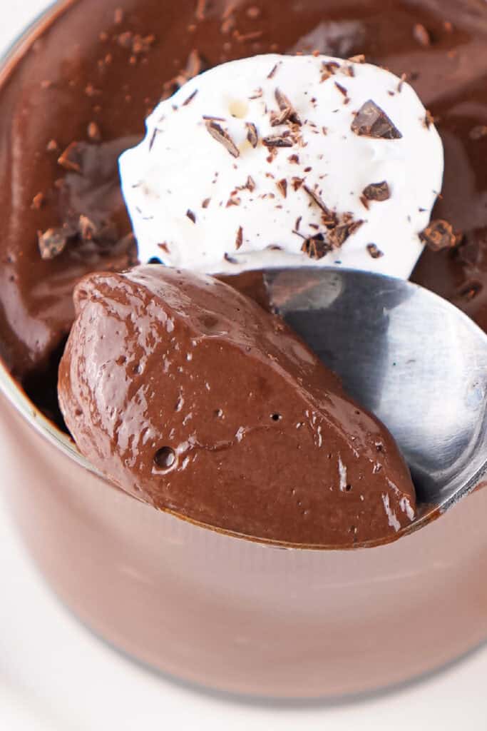 spoonful of chocolate pudding with whipped topping and chocolate shavings in a glass cup