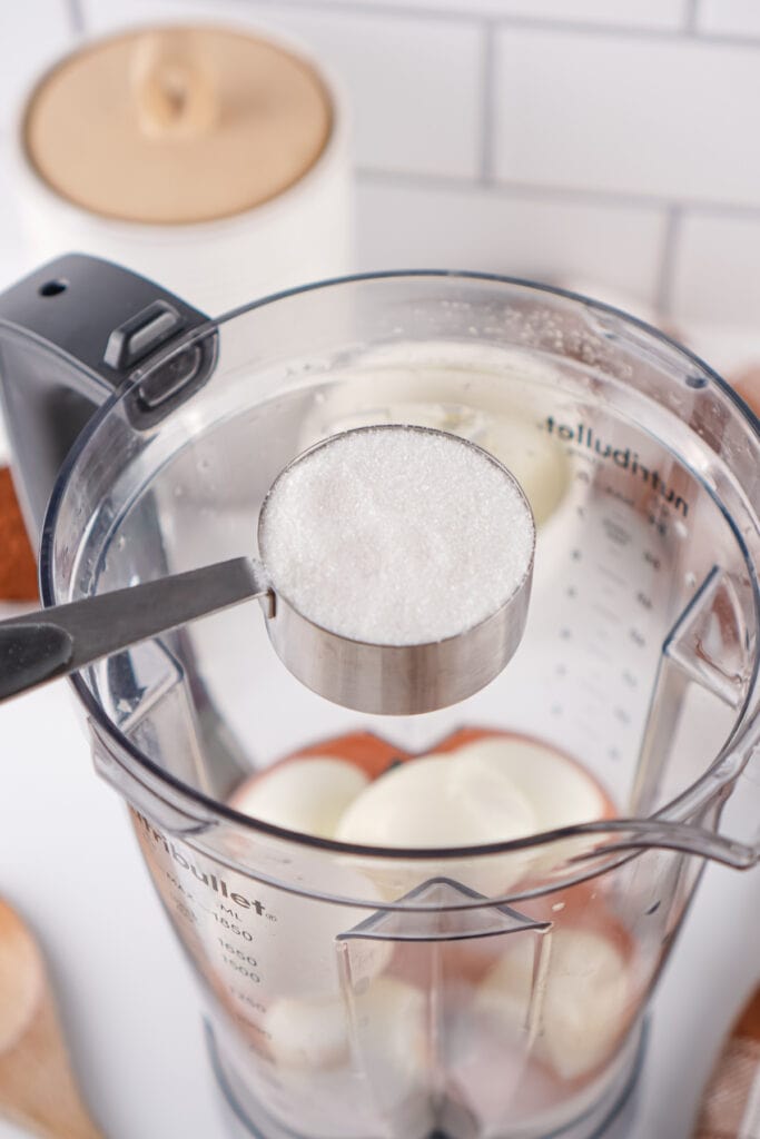 measuring cup of granulated sugar held over blender with hard boiled eggs inside