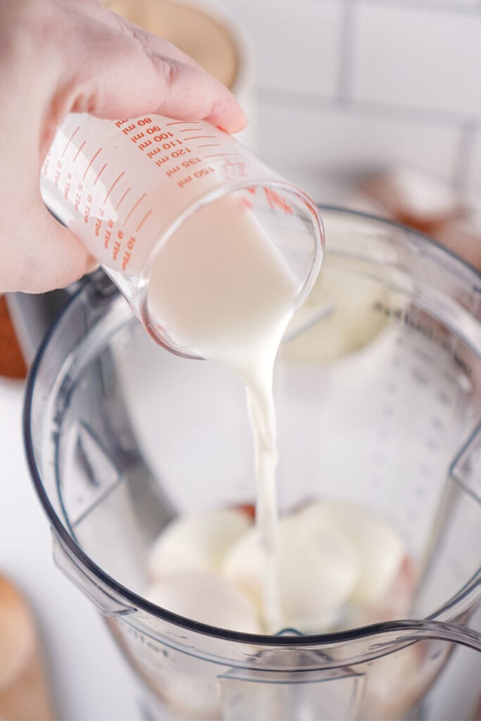milk being poured into a blender with hard boiled eggs