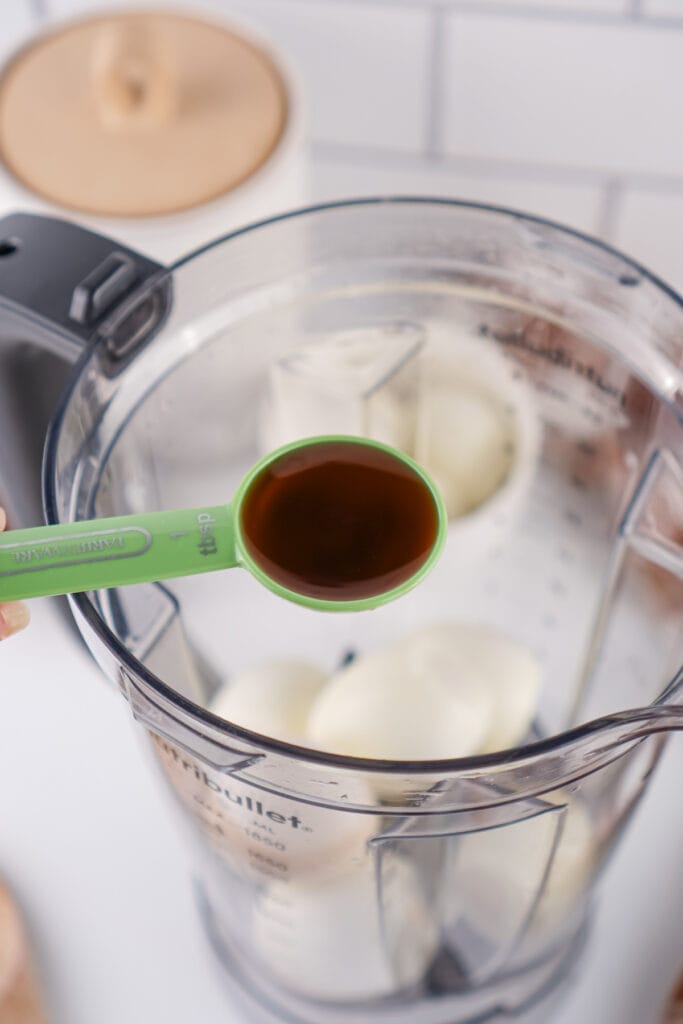 tablespoon of vanilla extract held over blender with hard boiled eggs inside