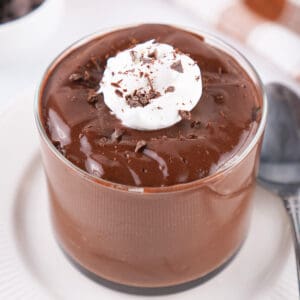 glass of chocolate pudding topped with whipped topping and chocolate shavings on a white plate