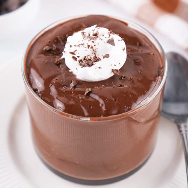 glass of chocolate pudding topped with whipped topping and chocolate shavings on a white plate