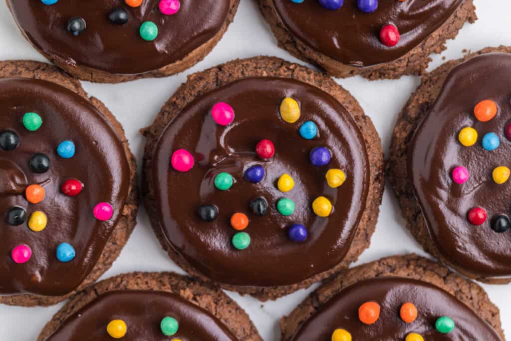 overhead view of multiple chocolate cookies with ganache and rainbow candy-coated chips