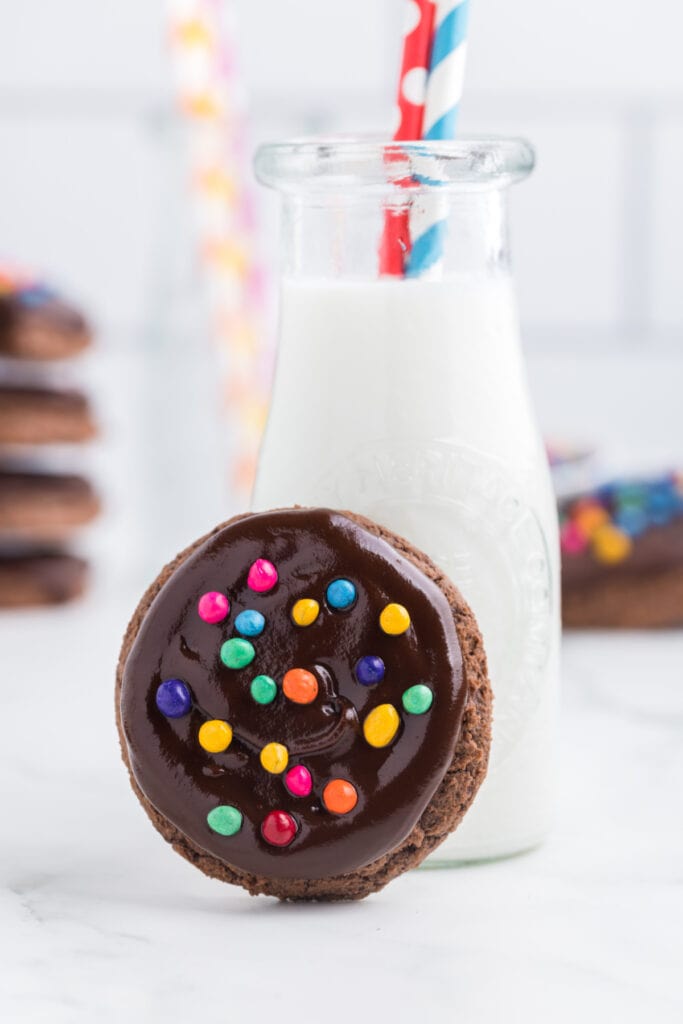 chocolate cookie leaning against a glass bottle of milk with a striped straw