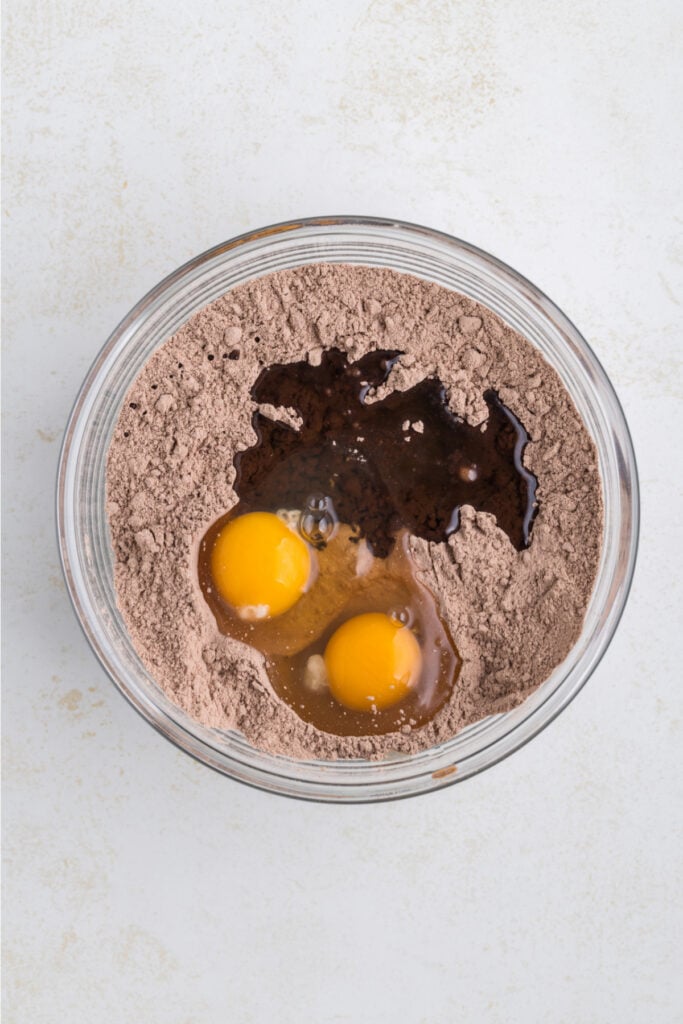 glass bowl with brownie mix, two eggs, and oil added on top