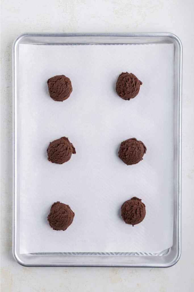 scoops of chocolate cookie dough spaced on a parchment-lined baking sheet