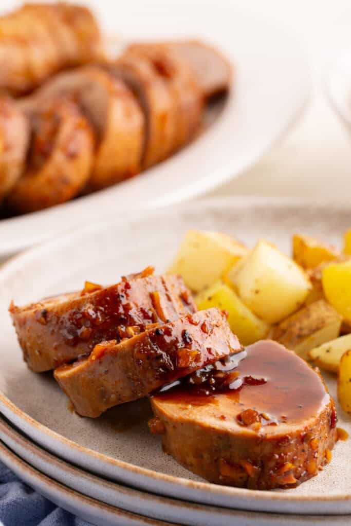 Sliced honey garlic pork tenderloin on a plate with roasted potatoes and glaze spooned over the top.