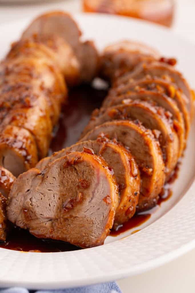 Close-up of sliced honey garlic pork tenderloin arranged on a white serving platter with sauce underneath.