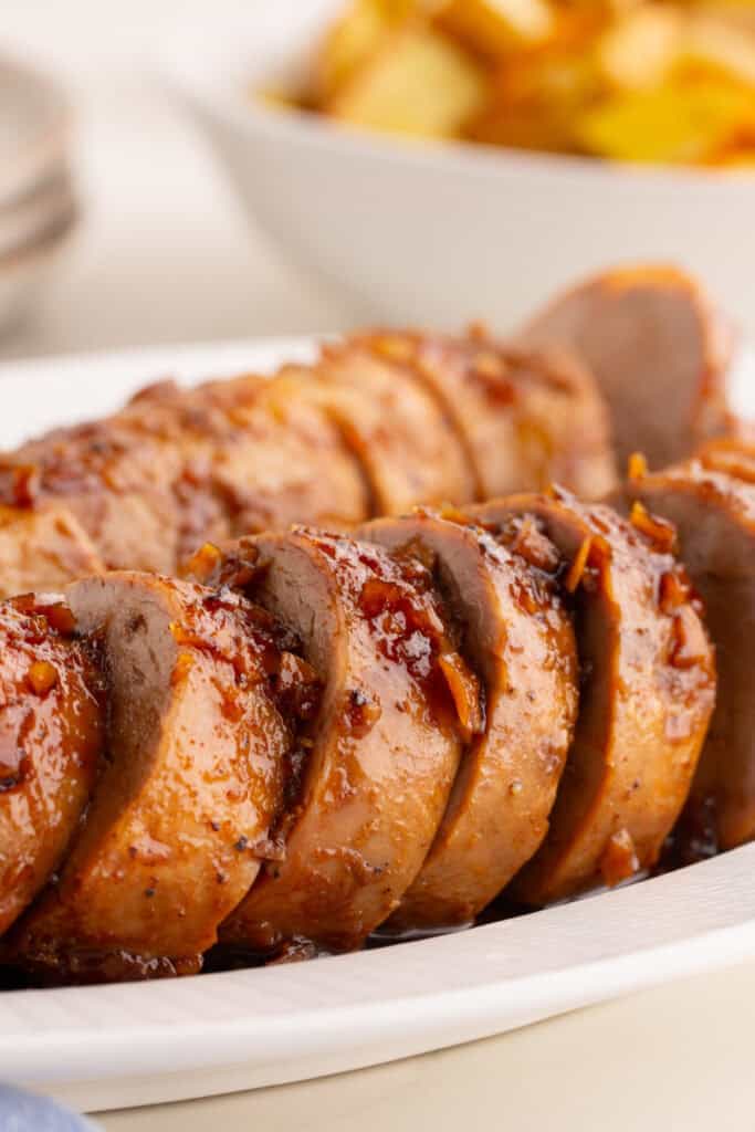 Close-up of sliced honey garlic pork tenderloin arranged on a white platter with glaze and minced garlic on top.