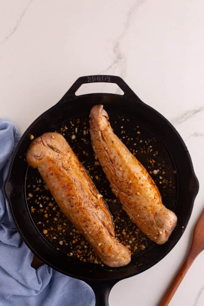 Two pork tenderloins in a cast iron skillet with honey soy glaze and minced garlic.