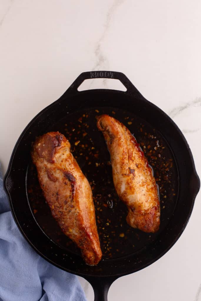 Pork tenderloins browning in a cast iron skillet with honey garlic sauce.