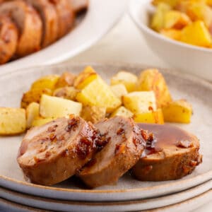 Sliced honey garlic pork tenderloin on a plate with roasted potatoes and glaze spooned over the top.