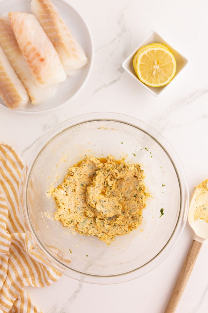 Glass bowl with garlic herb butter mixture fully combined, showing flecks of parsley and paprika throughout.
